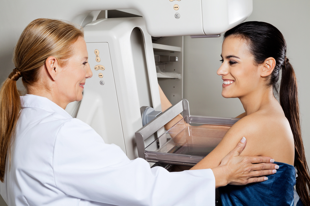 Mature female doctor assisting young patient during mammogram test.
