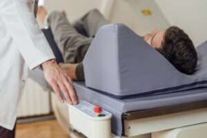 Hand of a medical technician operating the bone densitometer while his patient is lying on the bed.
